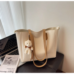 Detail of woven texture on cream tote bag with leather handles and teddy bear charm