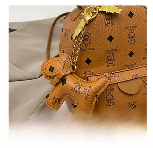 Detail of brown teddy bear leather charm with golden chain and luxury brand logo print