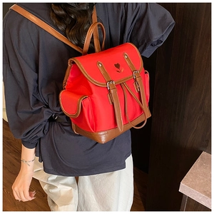 Detail of red nylon backpack with brown leather trim and floral embroidery on the flap