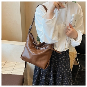 Detail view of large brown leather tote bag with metallic buckle and shoulder strap fit
