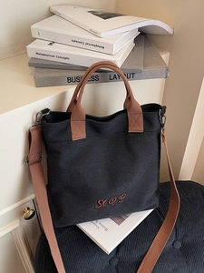 Minimalist black canvas tote bag with brown woven handles and adjustable shoulder strap