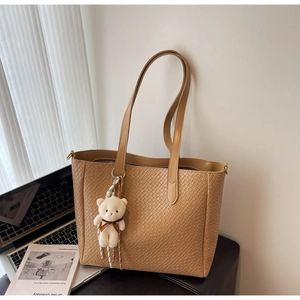 Detail of khaki woven texture tote bag featuring a cute white plush bear charm
