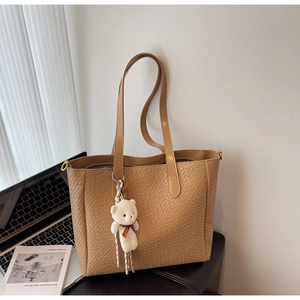 Detail of woven texture on a camel tote bag with a cute bear charm and laptop background