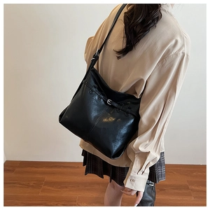 Side view of a black leather underarm tote bag with silver buckle worn with a casual outfit