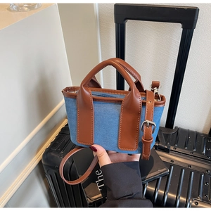 Detail of denim canvas mini tote bag with brown leather handles and silver hardware