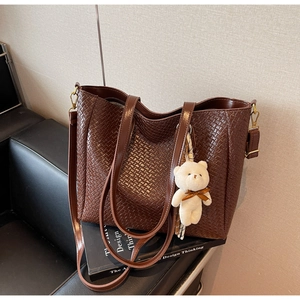 Detail of dark brown woven tote bag texture with a cute plush bear charm on a sofa