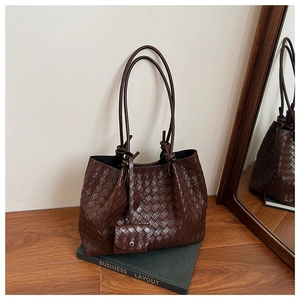 Detailed view of dark brown woven leather tote bag with small matching pouch on green book