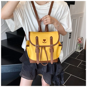 Detail of yellow canvas backpack with brown leather trim and heart embroidery accents