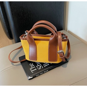 Detail of yellow canvas tote bag with brown leather trim and metal buckles on a book