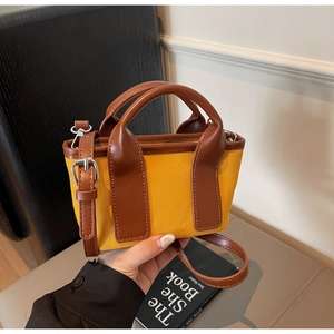 Detail of yellow canvas handbag with brown leather straps and metal hardware