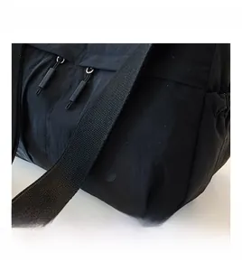 Detail of black nylon small crossbody bag featuring dual zippers and circular embossed logo