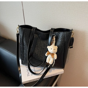 Detail of black woven tote bag featuring a cute plush bear charm on a leather sofa