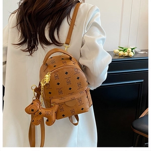 Detail of tan mini backpack with teddy bear pattern and cute charm on white blazer