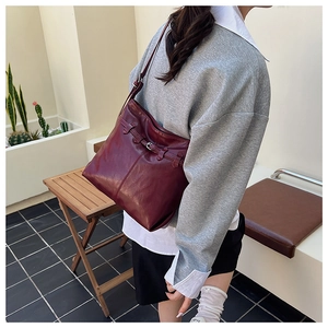 Detailed view of deep red leather shoulder bag featuring decorative silver metal buckle