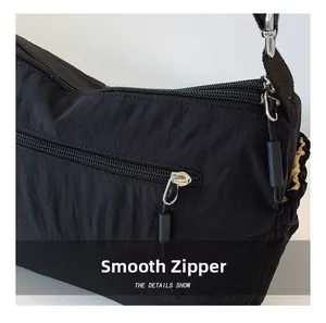 Detail shot of smooth double zippers on a black nylon crossbody bag with pleated texture