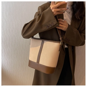 Detail view of canvas bucket bag with brown leather trim and white contrast stitching