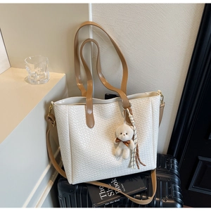 Close-up of white woven tote bag with brown leather strap and plush bear charm