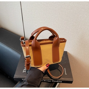 Detail of mini canvas and leather tote bag with brown straps on a book