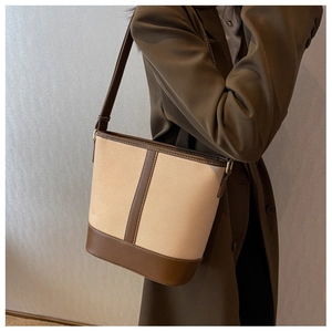 Detail of beige canvas bucket bag with brown leather trim worn by model in brown coat