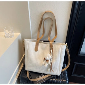 Detail of white woven tote bag with leather handles and bear charm on suitcase