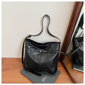 Detail of a large black faux leather tote bag with metallic buckle on a grey prop book