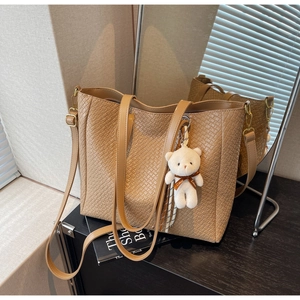Detailed view of the brown woven tote bag featuring a plush bear charm and straps