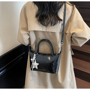 Dettaglio borsa nera lucida con ciondolo a stella argentata su un trench beige