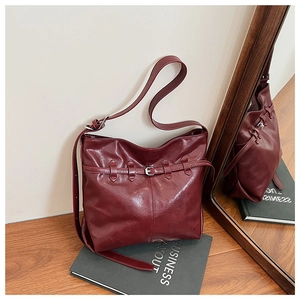 Detail showing high-gloss wine red leather tote bag with vintage buckle on wooden desk
