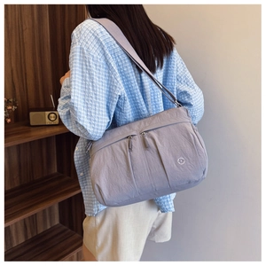 Detail of light purple nylon shoulder bag with multiple pockets and metal logo on strap