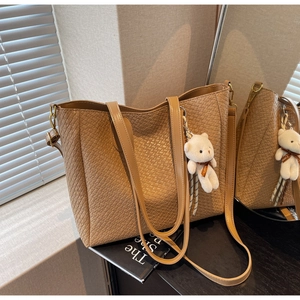 Detail of tan woven tote bag with glossy straps and cute plush bear accessory