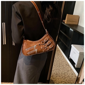 Detail of vintage brown crossbody bag with punk metal buckles and rivets on moon-shaped PU leather