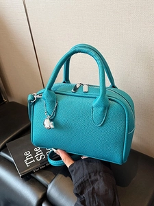 Teal lychee pattern leather bowling bag with silver dolphin pendant on a leather chair
