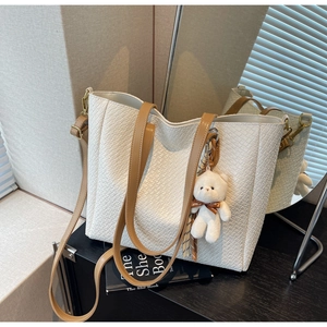 Detailed close-up of a white croc-embossed tote bag with a cute plush bear pendant