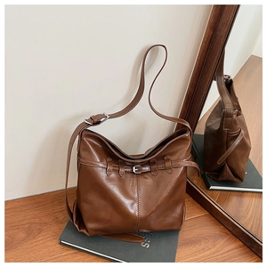Detail of dark brown vintage leather hobo bag with metal buckle on a rustic desk