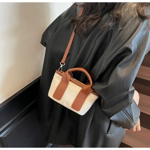Detail of canvas bag with brown leather trim and silver metal clasps on a model