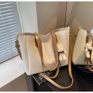 Close-up of beige woven tote bag with brown handles and a cute bear pendant charm