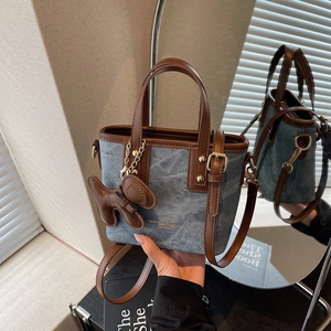 Blaue Denim-Tragetasche mit braunem Lederbesatz und Welpen-Anhänger auf einer Spiegelfläche
