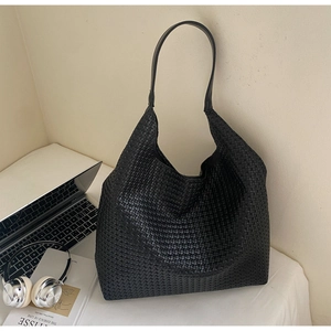 Detail of black woven leather tote bag texture on a white office desk with laptop
