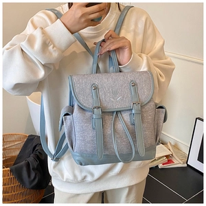 Detail of light blue patchwork backpack with dual buckles and floral embroidery on flap