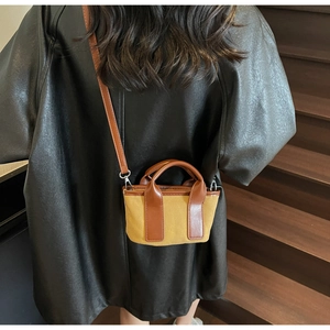 Detail of crossbody canvas bag with brown leather handles worn by model on stairs