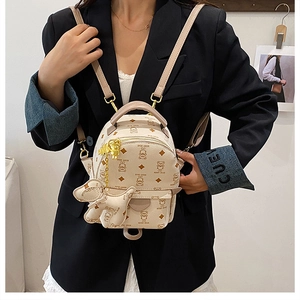 Detail of cream mini backpack with teddy bear pattern and plush dog charm worn by model