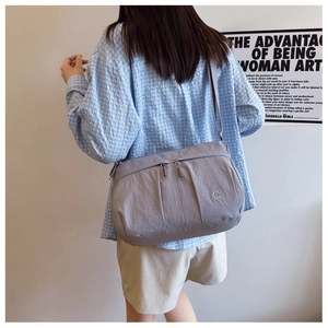 Detail of grey lightweight nylon crossbody bag with multi-zipper layers and brand logo