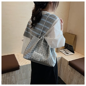 Detail of silver woven tote bag with a matching drawstring pouch on a model shoulder