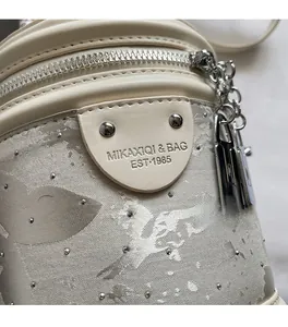 Détail du sac seau en cuir crème avec tissu jacquard à paillettes et breloque chaîne