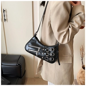 Detail of a black punk crescent bag with silver zippers and belt buckles on a model