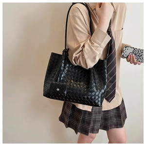 Model wearing a large black woven leather tote bag with a minimalist commuter aesthetic