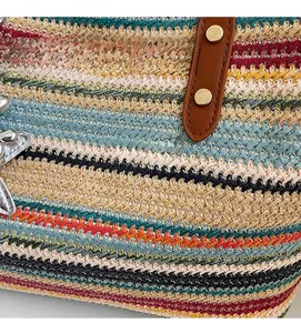 Detail einer bunten Strohtasche mit braunen Lederriemen und goldenen Metallnieten