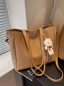 Brown woven leather tote bag with long straps and a plush bear pendant accessory