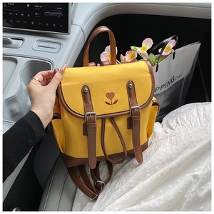 Close-up of yellow canvas backpack featuring heart embroidery and leather buckle straps