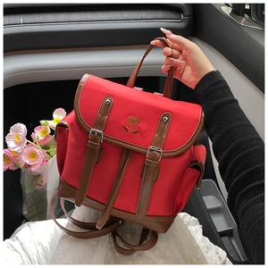 Detail of red nylon backpack featuring vintage heart embroidery and brown leather buckles